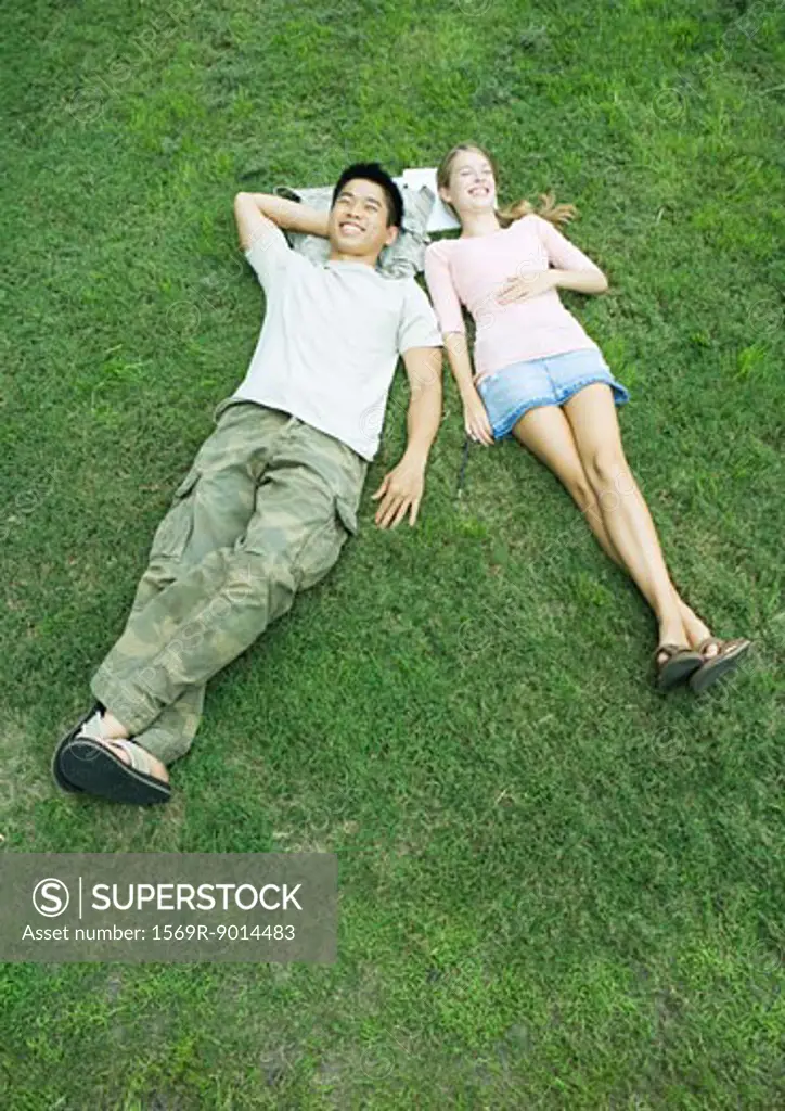 Young couple lying in grass with heads resting on books, high angle view