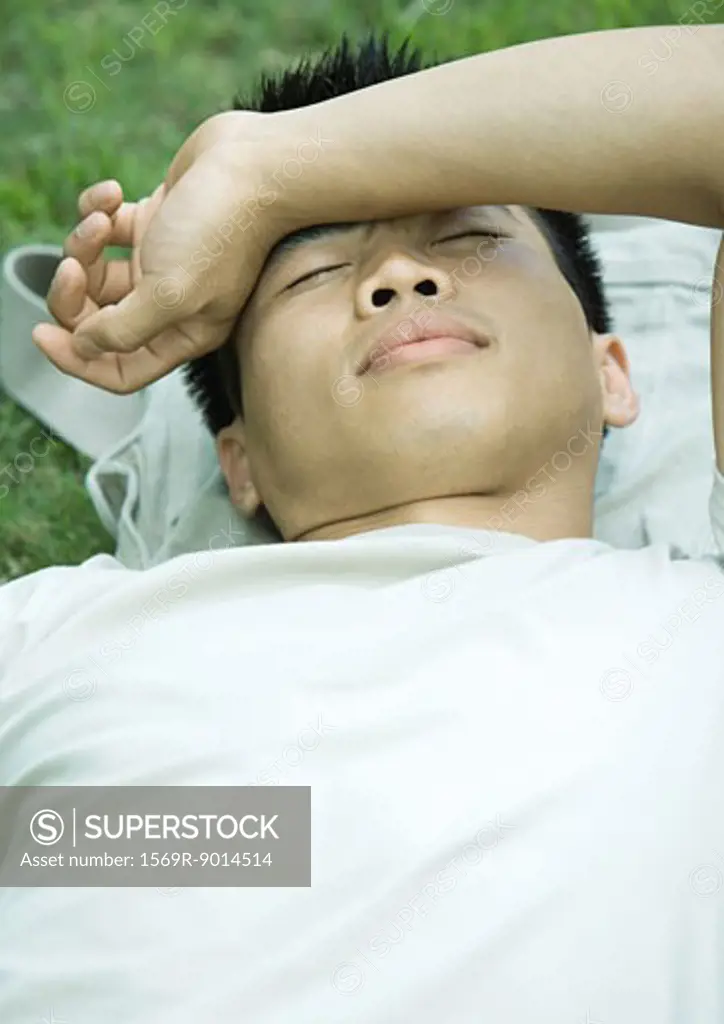 Young man lying in grass with arm across forehead