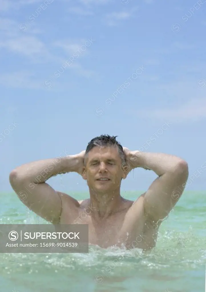 Man emerging from water, hands behind head