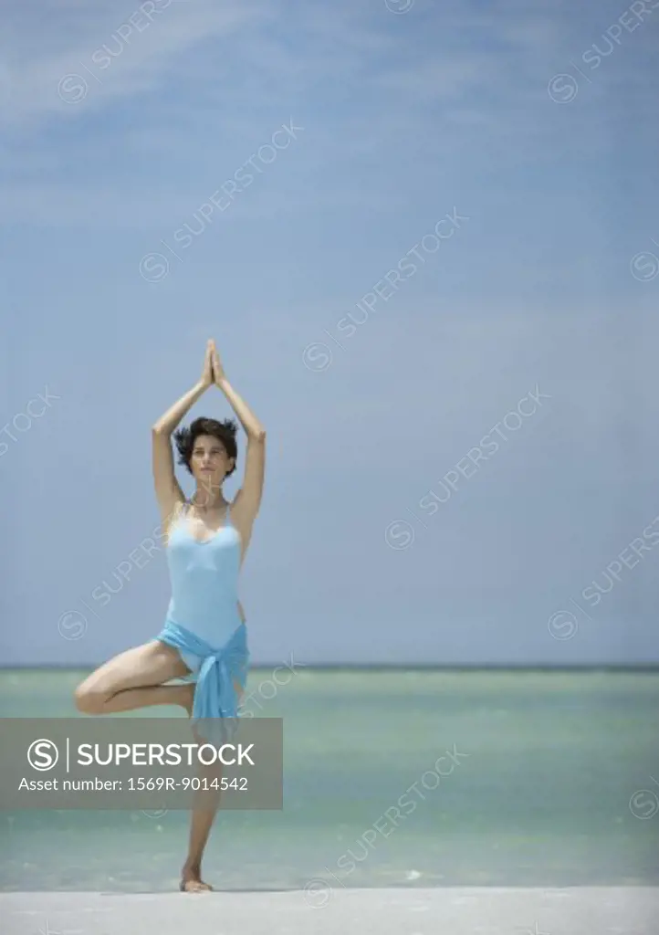 Woman standing on beach in yoga tree pose