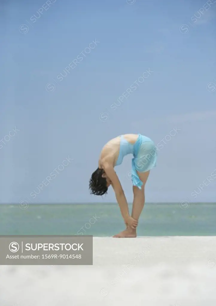 Woman bending over, holding ankles, on beach