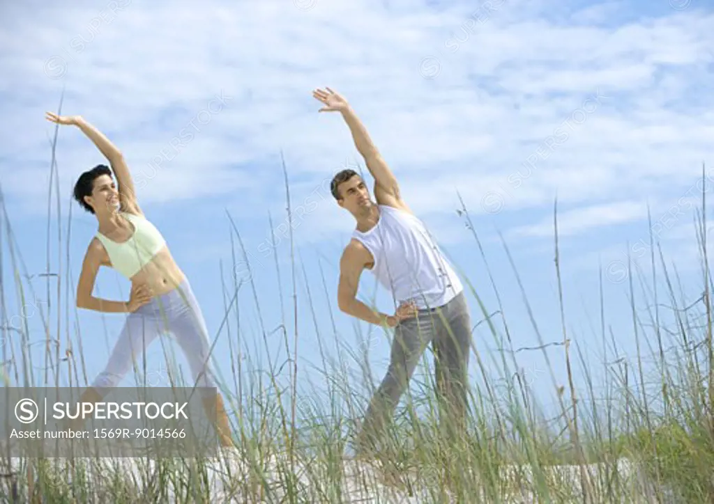 Man and woman doing side stretches on beach