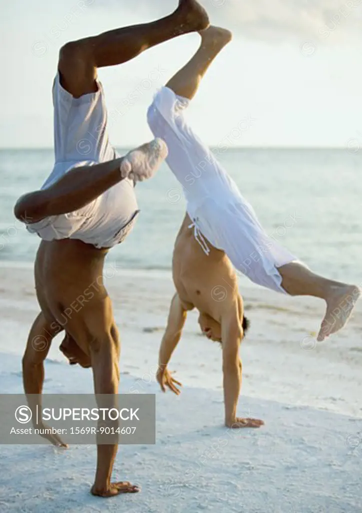 Two men turning cartwheels on beach