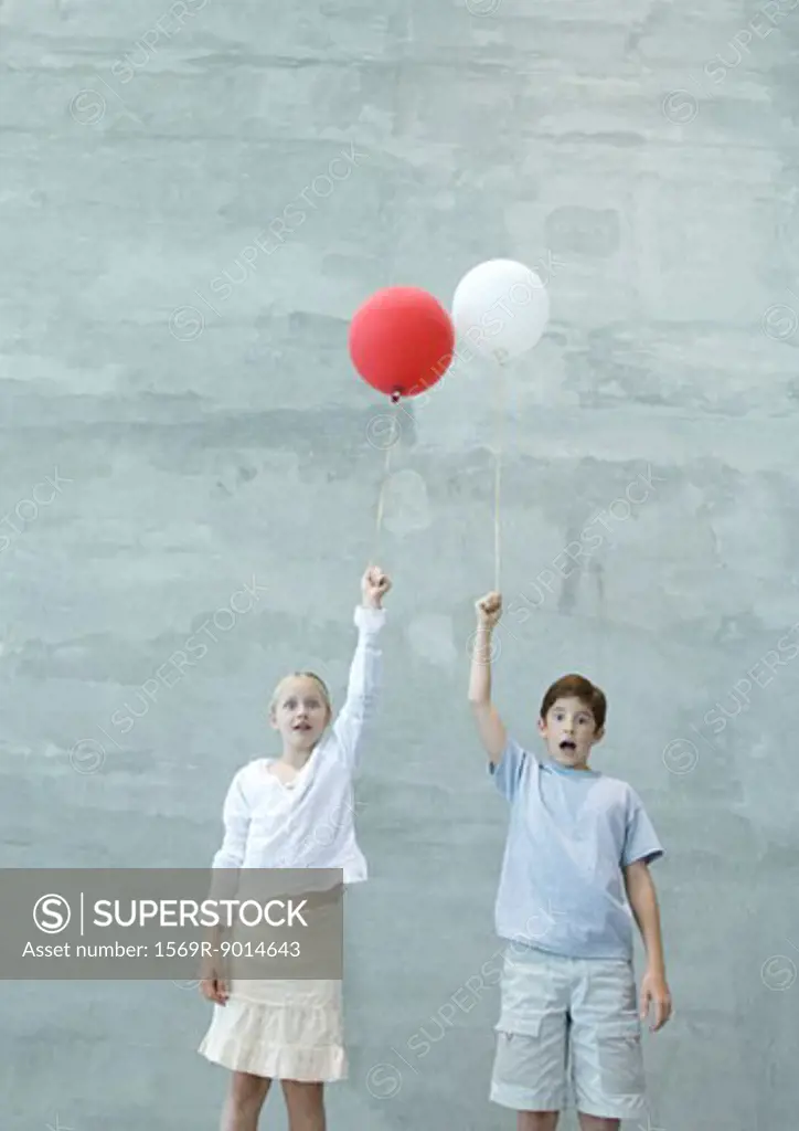 Two children holding balloons, making faces