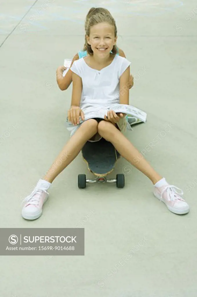 Two girls sitting back to back on skateboard, reading