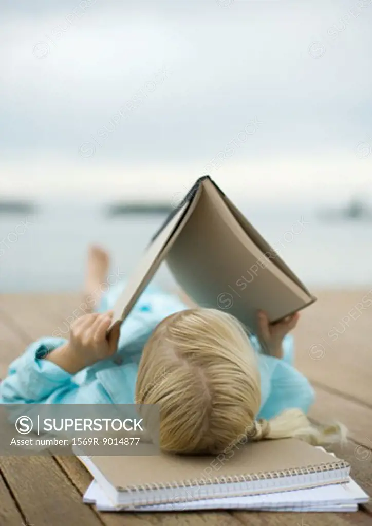 Girl reading book on dock