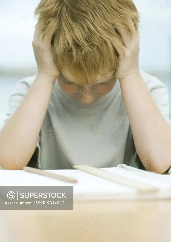 Boy holding head and looking down at homework