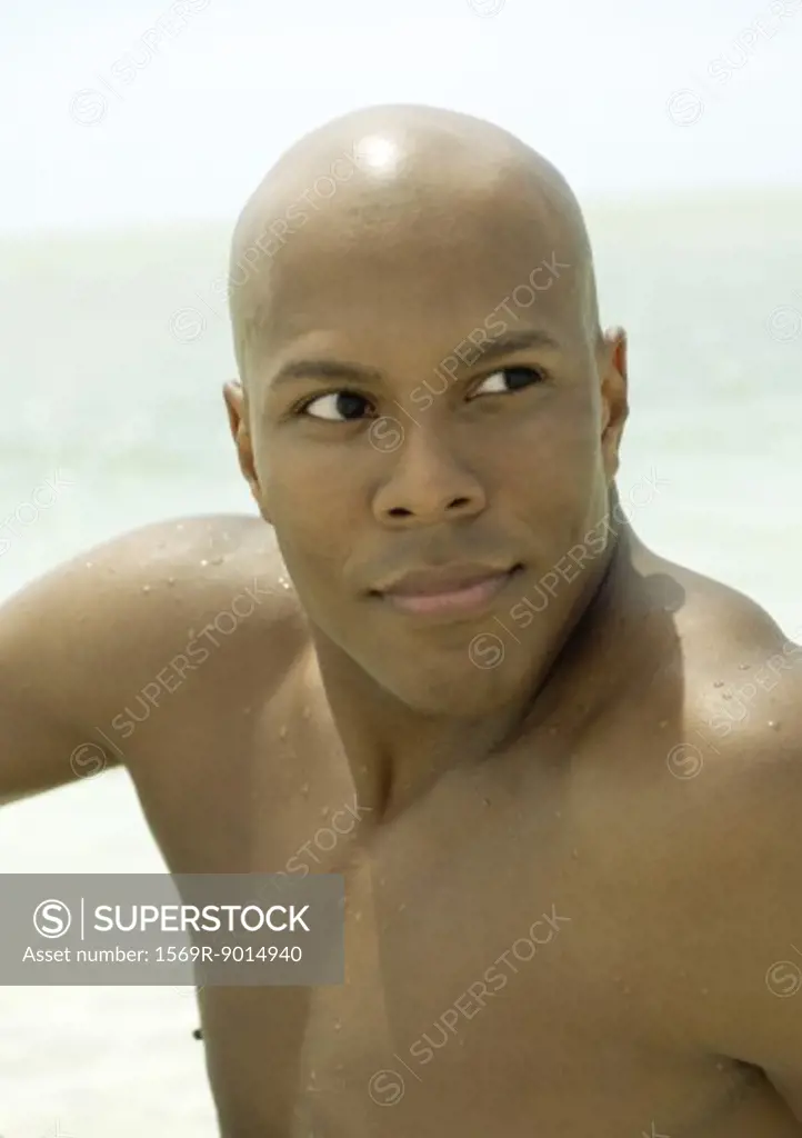 Barechested man, sea in background, looking away
