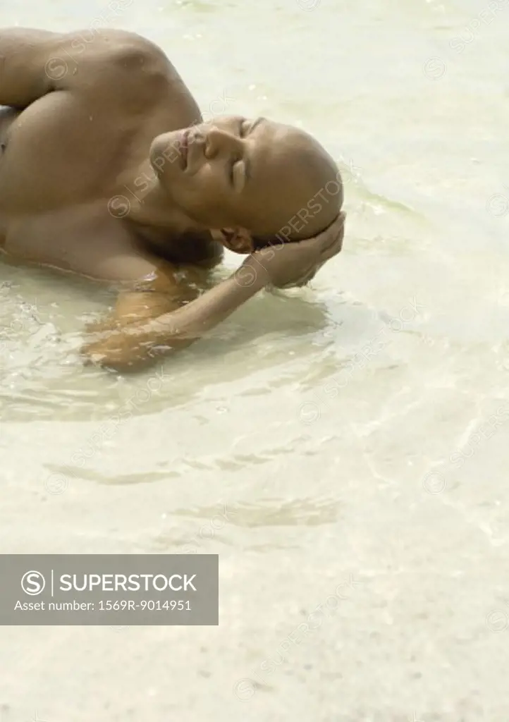 Man lying in shallow water with eyes closed