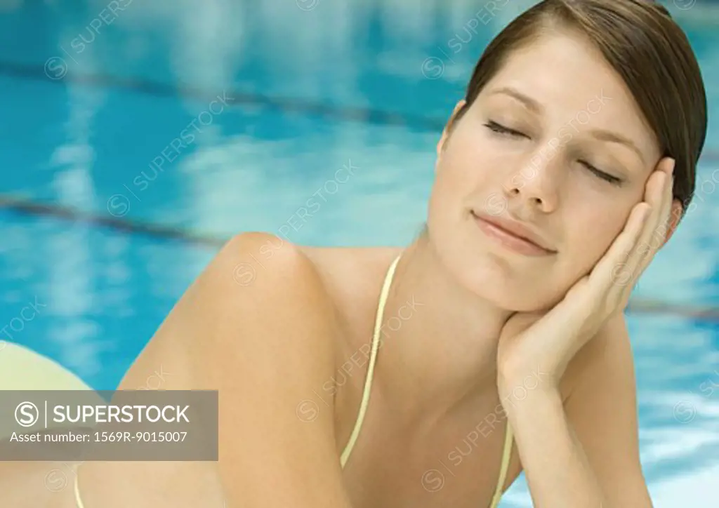 Woman lounging by pool, eyes closed
