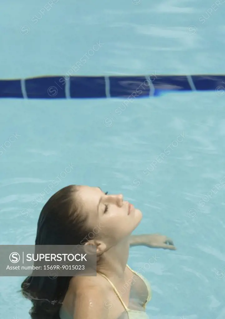 Woman standing in pool, head back and eyes closed, side view
