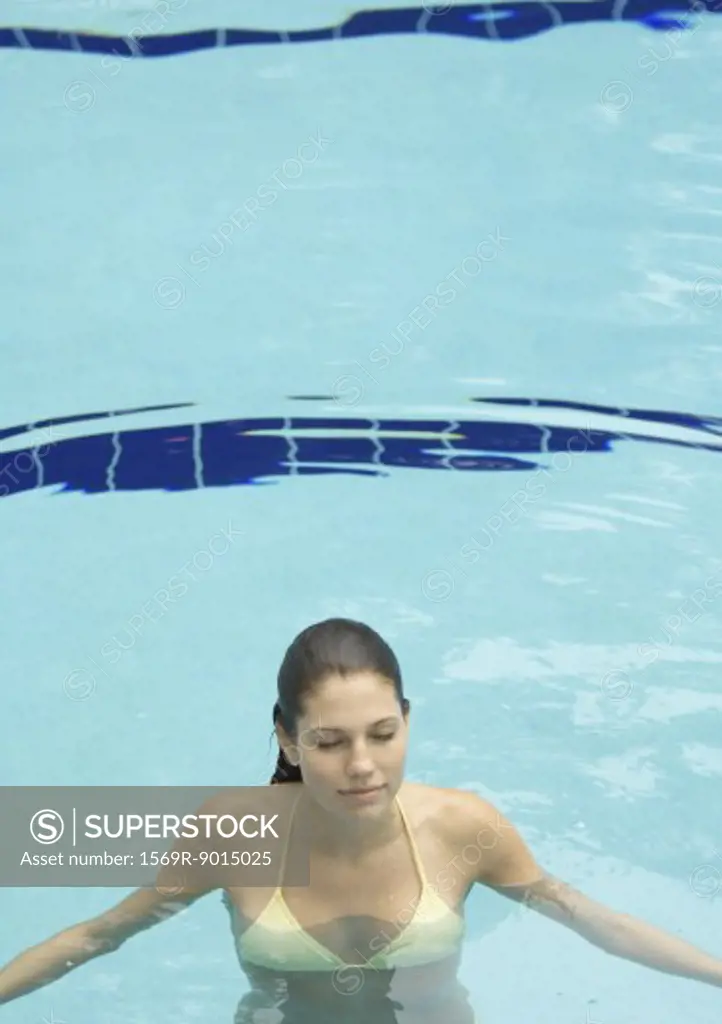 Woman standing in pool, eyes closed, front view