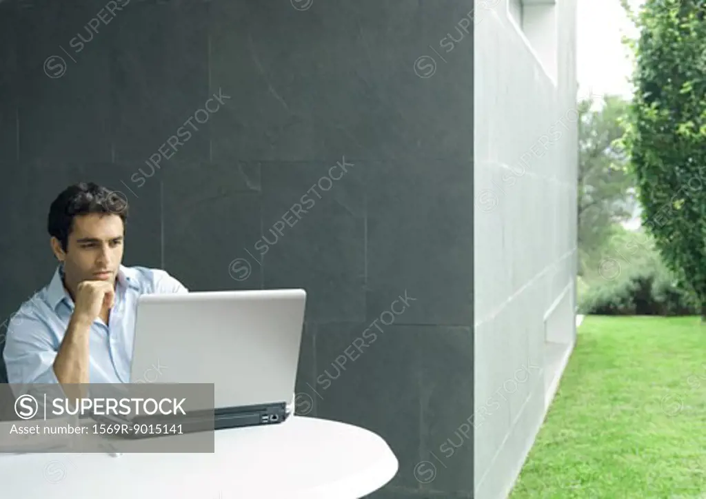 Man sitting at table outdoors, using laptop