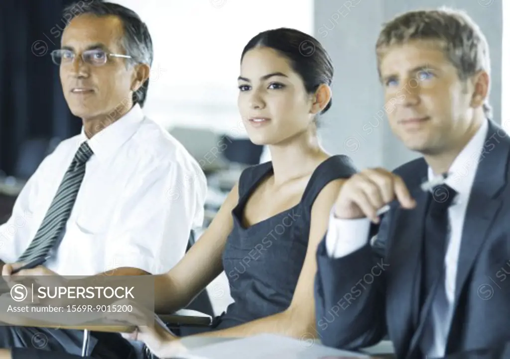 Businesspeople sitting holding, looking attentively out of frame