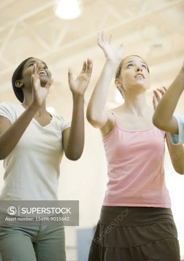 Teenage girls holding arms up to hit ball