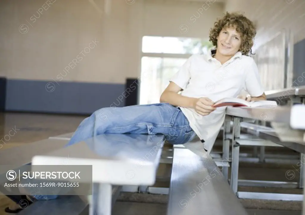 Teenage boy sitting on bleachers in school gym, studying