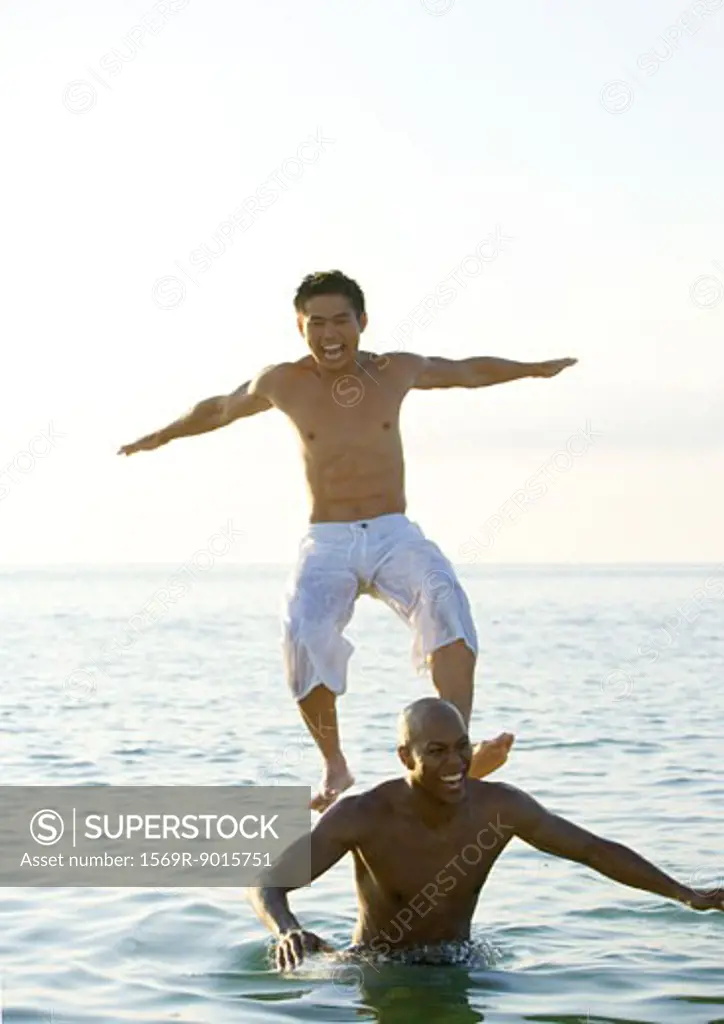 In sea, man standing on second man's shoulders is losing balance