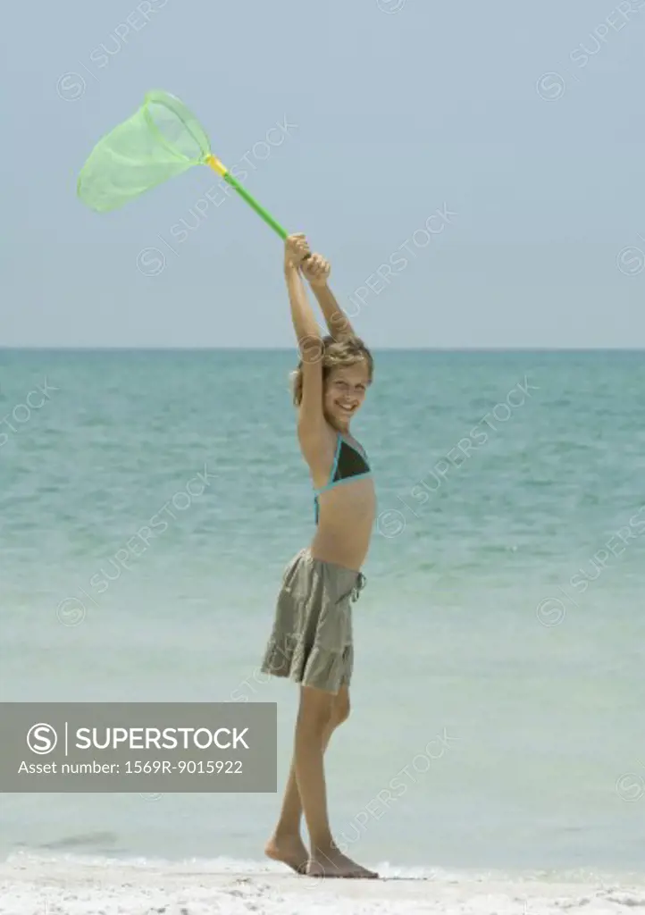 Girl on beach, holding up fishing net overhead - SuperStock
