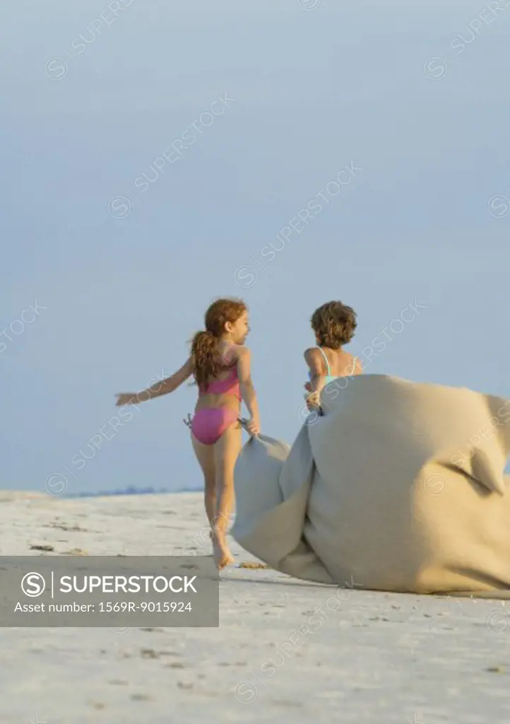 Two girls carrying blanket in wind on beach
