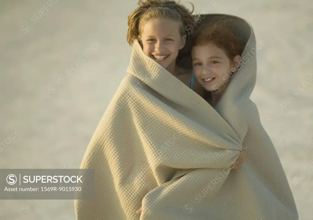 Two girls wrapped in blanket on beach