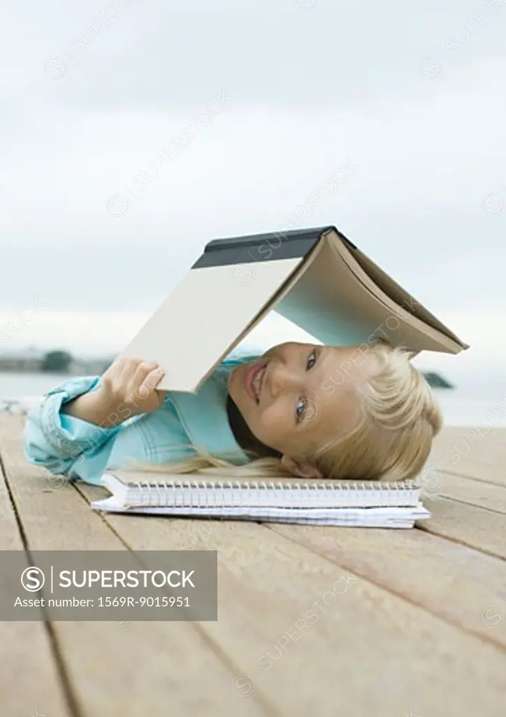 Girl lying on dock with book over head