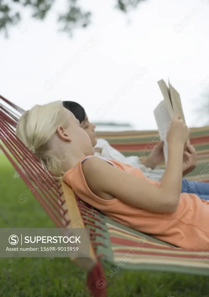 Girls lying in hammock reading book together