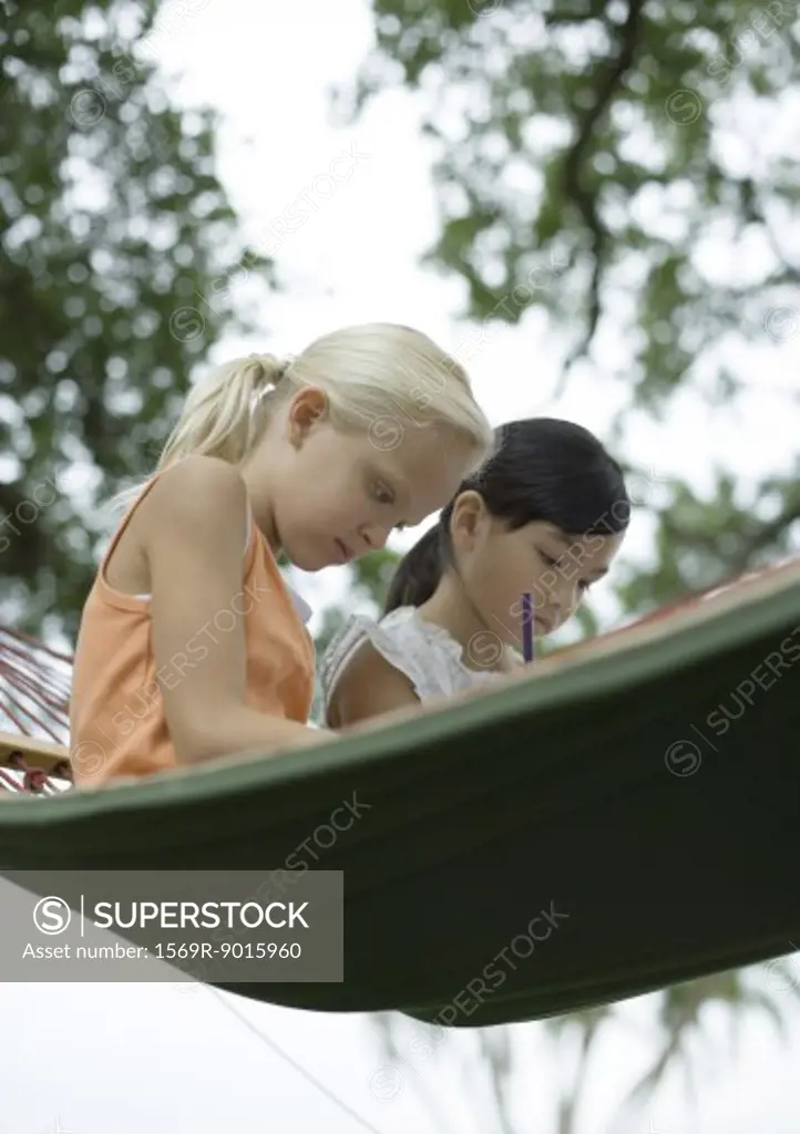 Two girls sitting in hammock, writing