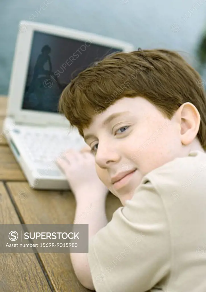 Boy using laptop, looking over shoulder at camera