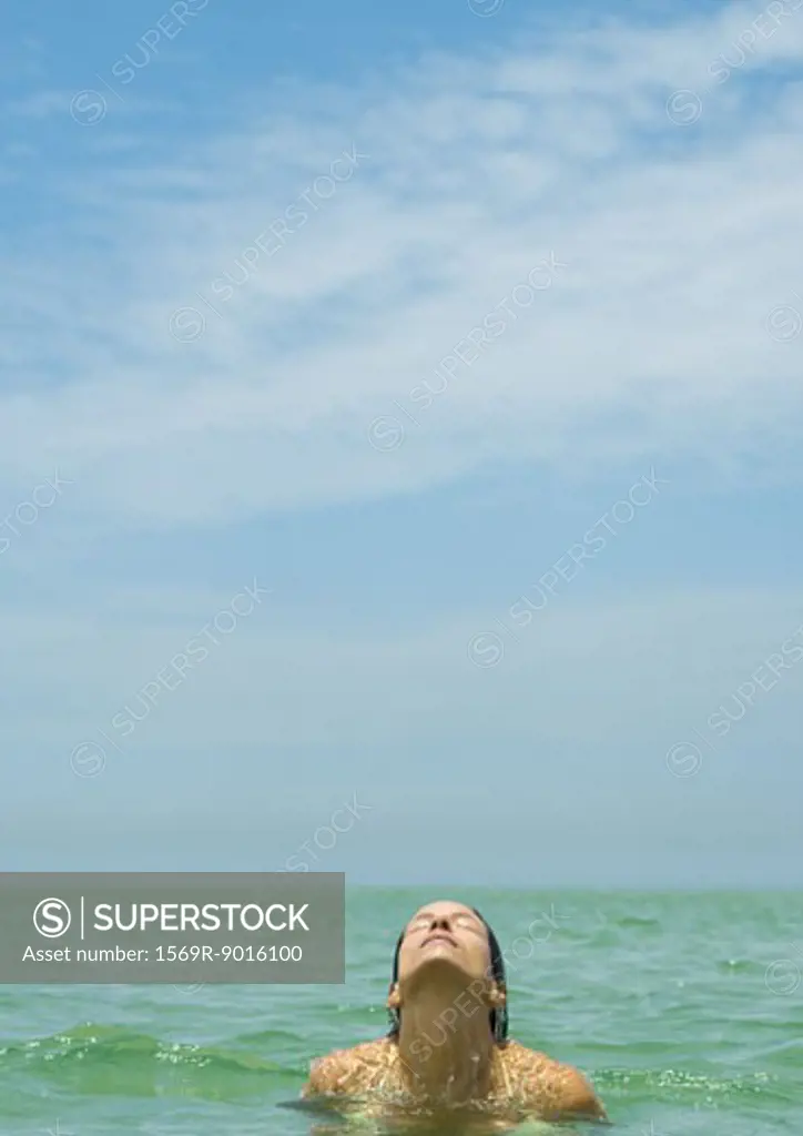 Woman standing in sea, head back and eyes closed