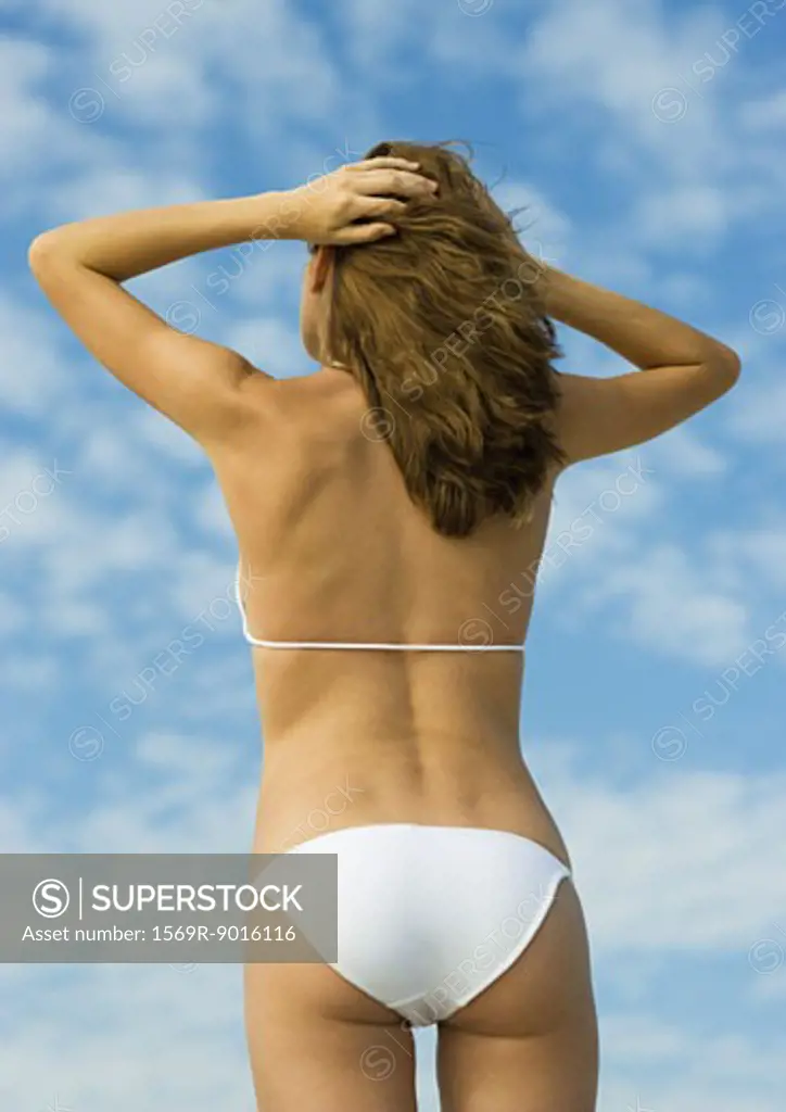 Woman in bikini standing with hands in hair, low angle rear view