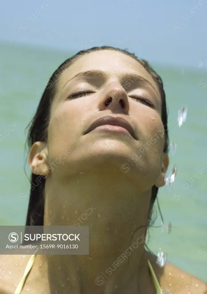 Woman with head back and drops of water in the air, sea in background