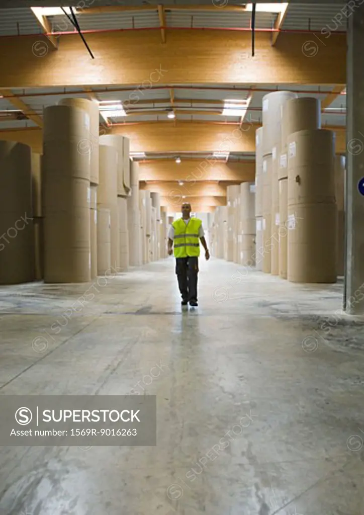 Man walking through rolls of paper in warehouse