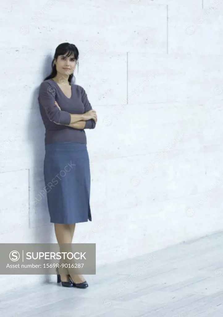 Businesswoman standing, leaning against wall, full length