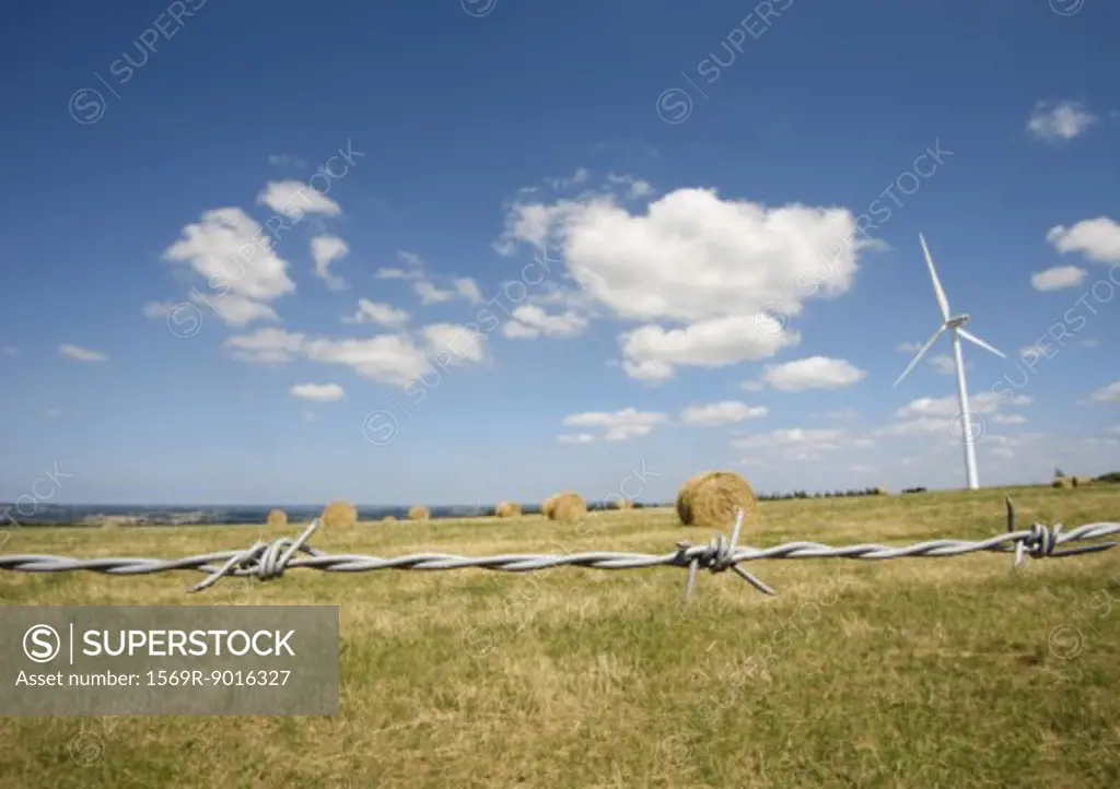 Wind turbine in field with bales of hay, barbed wire in foreground