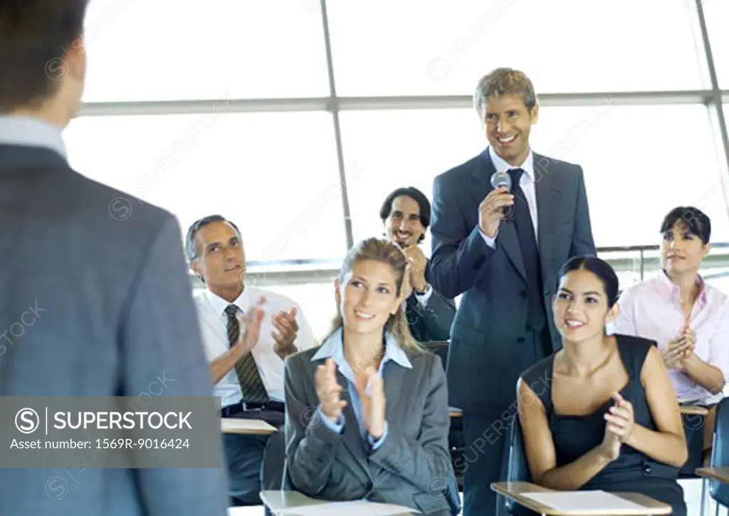 Executives in seminar, one man holding microphone, others clapping