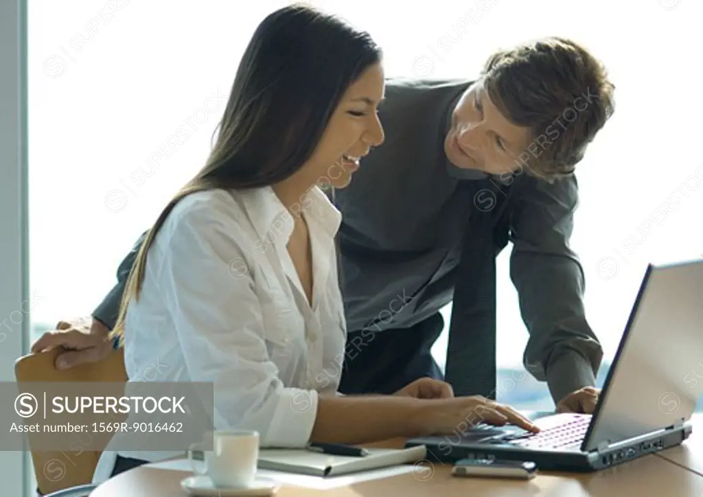 Female office worker using computer, businessman leaning over her shoulder