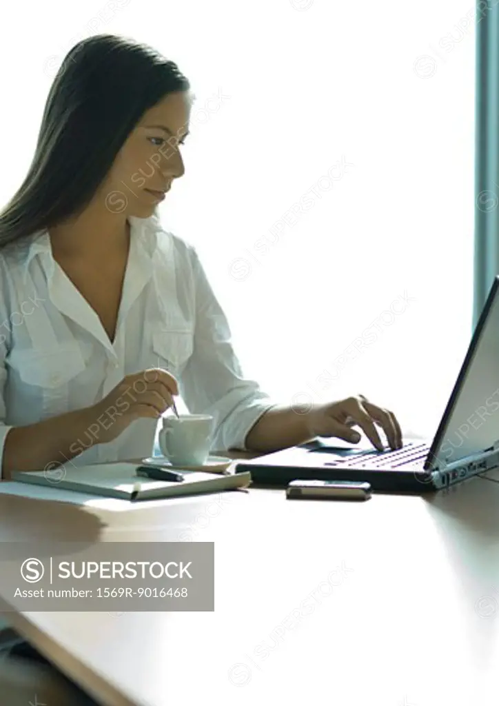 Businesswoman using laptop and stirring coffee