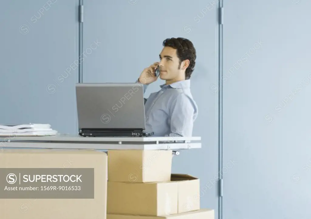 Businessman using cell phone, sitting at table top supported by cardboard boxes