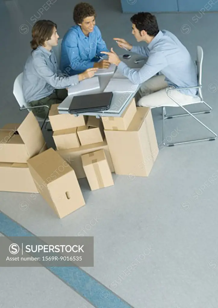 Businessmen sitting at table top supported by cardboard boxes, high angle view