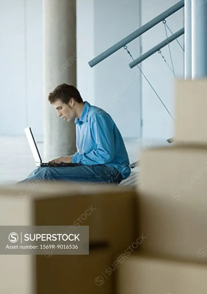 Businessman using laptop, cardboard boxes in foreground