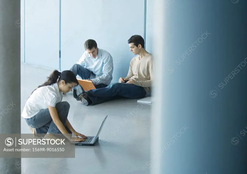 Young woman and two young men using laptops on floor