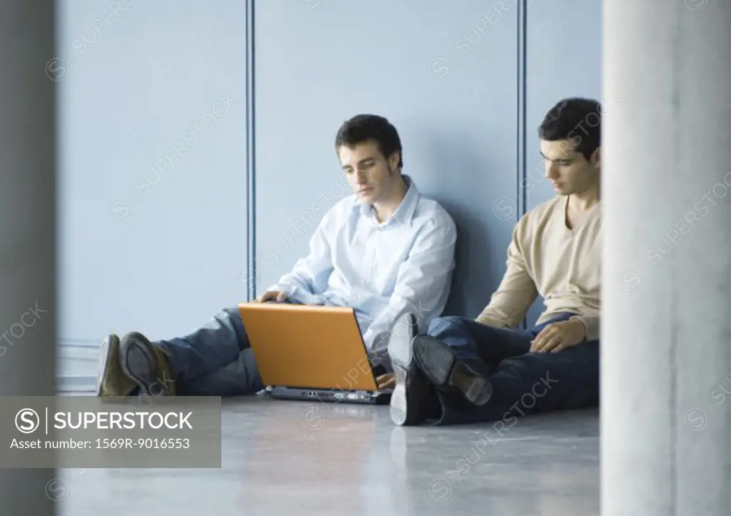 Two young businessmen, sitting on floor, using laptop
