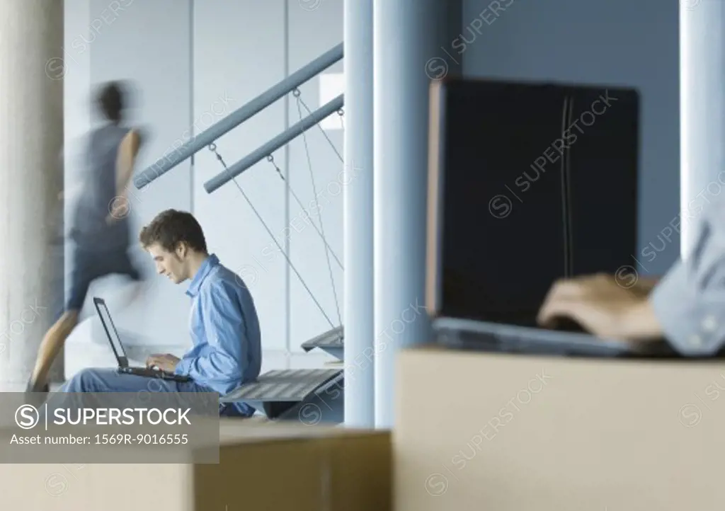 Businessman using laptop, second person using laptop on cardboard box in blurred foreground