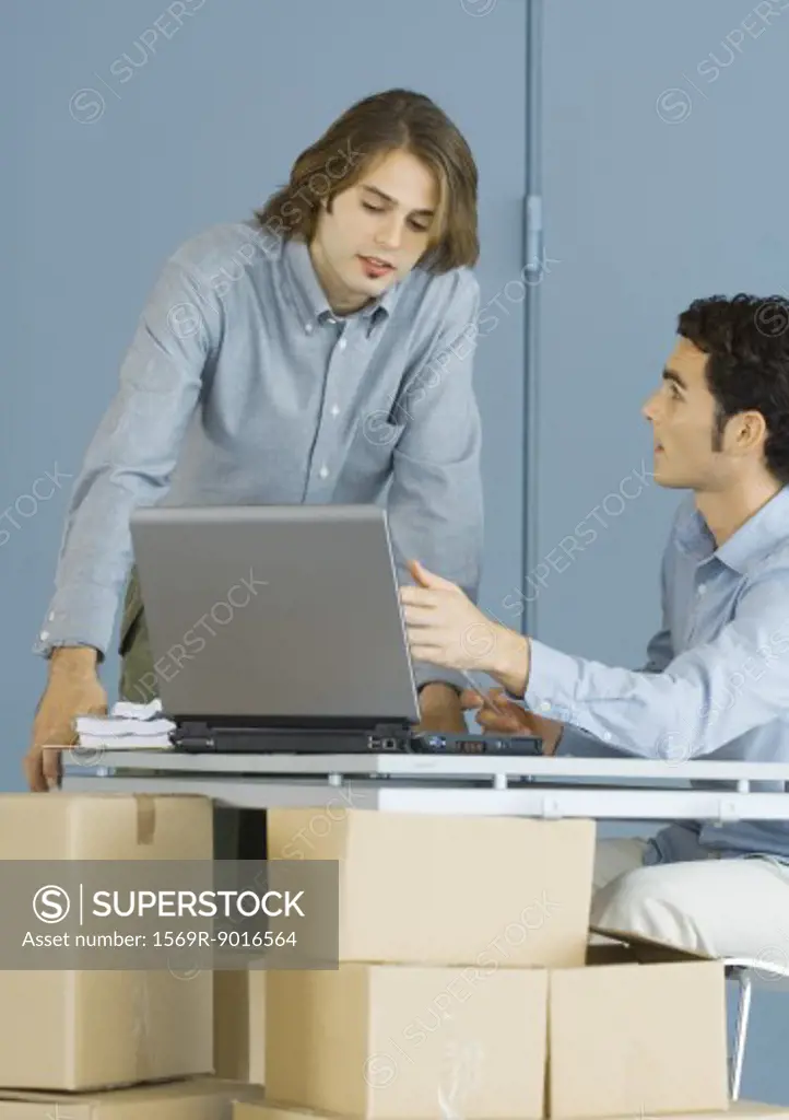 Businessmen using laptop, sitting at table top supported by cardboard boxes