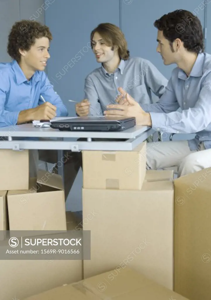 Businessmen talking, sitting at table top supported by cardboard boxes