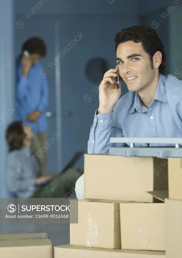 Young businessman using cellphone, sitting at table supported by cardboard boxes