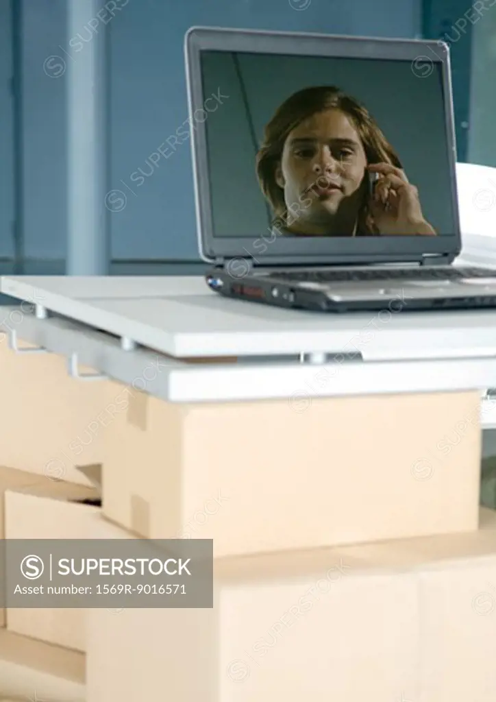 Image of man on laptop screen, laptop on table supported by cardboard boxes