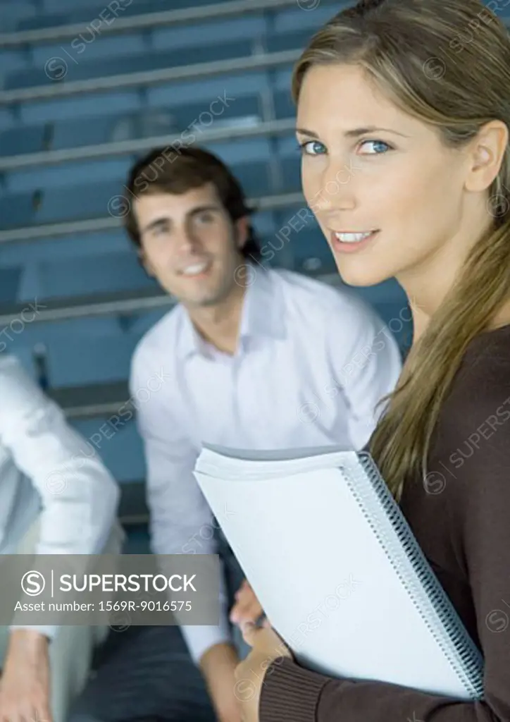 Young businesswoman holding notebook, colleagues in background