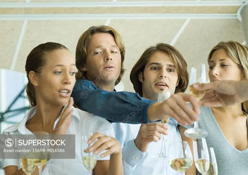 Man reaching over friends' shoulders for glass of champagne