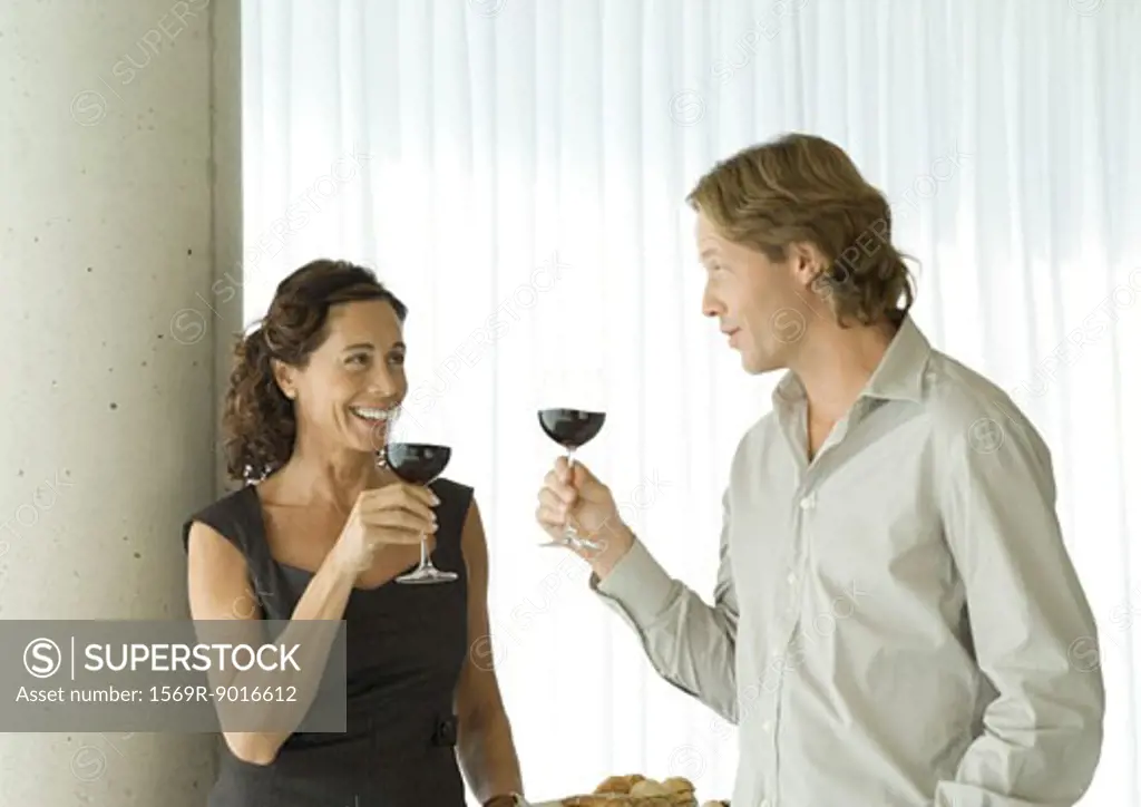 Man and woman standing with glasses of red wine, chatting